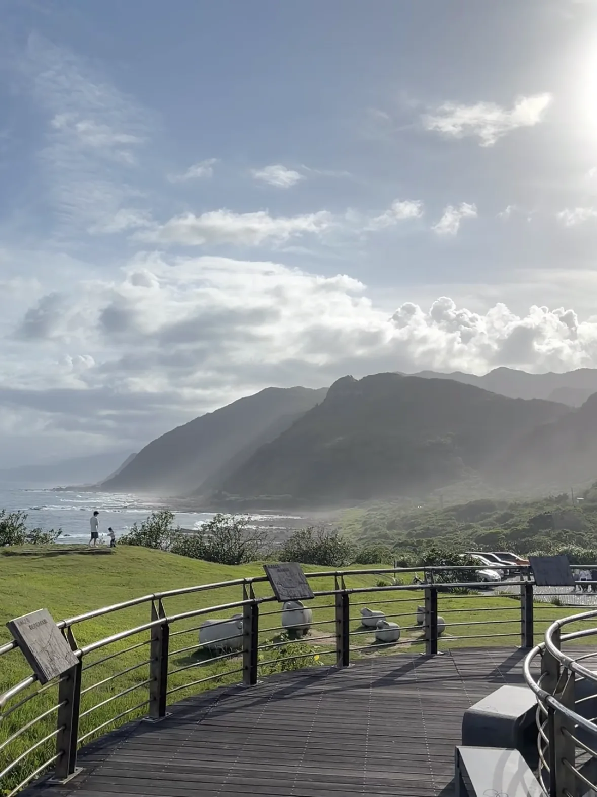 Wooden boardwalk viewing platform above green headlands and surf on Taiwan's northeast coast, late afternoon light through sea mist