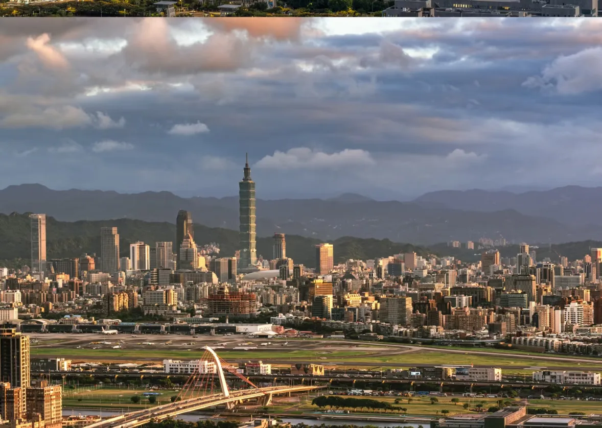The Taipei basin at dusk from a mountain ridge, Taipei 101 and the skyline catching the last warm light beyond the river bridges