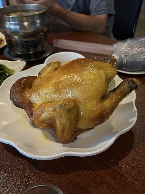 A golden roast chicken on a white plate at a round wooden table set for a Taiwanese family meal